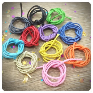 May include: Assortment of 10 spools of colorful waxed cotton cord. The cords are arranged in a circle on a wooden surface. The colors include black, gray, red, purple, green, blue, yellow, orange, beige, and pink.
