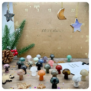 May include: A Christmas advent calendar with a brown paper background and a white inscription that reads "Oh, it is almost Christmas". The calendar has 24 numbered windows, each containing a small crystal mushroom. The mushrooms are in various colours and shapes, including clear, pink, green, blue, and brown. There are also three crystal ornaments hanging from the top of the calendar: a star, a crescent moon, and a star.