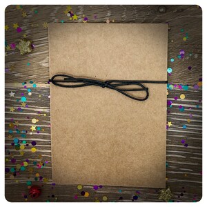 May include: A brown paper card with a black string tied around it. The card is on a wooden surface with colorful confetti scattered around it.
