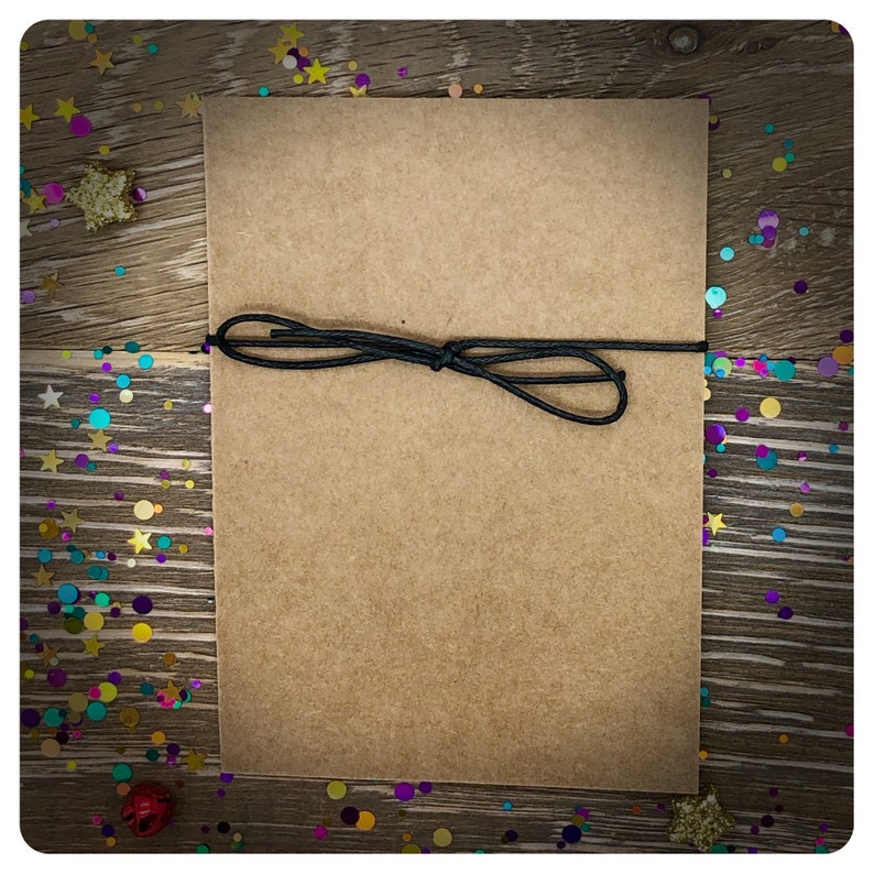 May include: A brown paper card with a black string tied around it. The card is on a wooden surface with colorful confetti scattered around it.