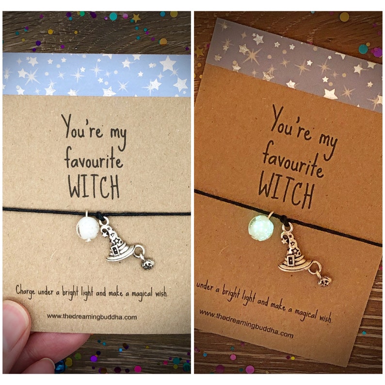 May include: Two cards with the text "You're my favorite WITCH" and a witch hat charm on a black string. The cards have a blue and white star pattern on the top and the text "Charge under a bright light and make a magical wish. www.thedreamingbuddha.com" on the bottom.