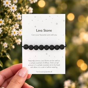 May include: A black lava stone bead bracelet displayed on a white rectangular card. The card features the text Lava Stone, Carry your favourite scent with you, and instructions for using the beads as an essential oil diffuser, plus The Dreaming Buddha logo.