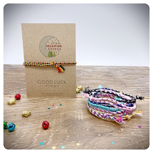 May include: A stack of colorful friendship bracelets with a card that says "Good Luck You Can Do It" and a logo that says "The Dreaming Buddha".