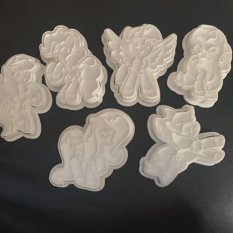 Puede incluir: Un conjunto de cortadores de galletas de pl&aacute;stico blanco con dise&ntilde;os de ponis. Los cortadores presentan contornos detallados de los personajes, incluido uno con alas. Ideales para crear galletas tem&aacute;ticas.