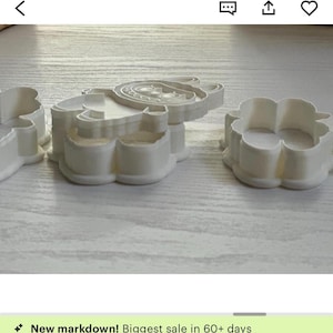 Puede incluir: Cortadores de galletas de pl&aacute;stico blanco con forma de oso, flor y otra forma. El cortador de oso tiene rasgos faciales detallados. Los cortadores est&aacute;n sobre una superficie de madera de color claro.