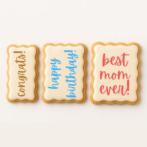 May include: Three decorated sugar cookies with different messages. The first cookie says "congrats!" in brown lettering. The second cookie says "happy birthday!" in blue lettering. The third cookie says "best mom ever!" in red lettering.