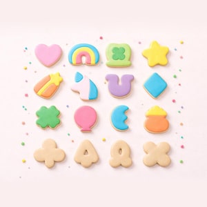 May include: A collection of colorful, frosted sugar cookies in various shapes, including a heart, rainbow, shamrock, star, and unicorn. The cookies are arranged on a light pink surface with colorful sprinkles.