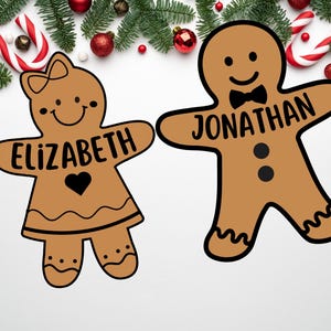 Peut inclure: Deux personnages en pain d'&eacute;pices, l'un avec le nom "Elizabeth" et l'autre avec le nom "Jonathan", sont d&eacute;cor&eacute;s de gla&ccedil;age noir et entour&eacute;s de d&eacute;corations de No&euml;l.