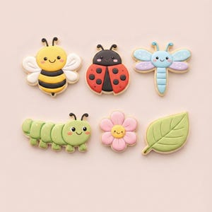 Peut inclure: Six biscuits décorés en forme d'abeille, de coccinelle, de libellule, de chenille, de fleur et de feuille. Les biscuits présentent des couleurs vives et des visages souriants, parfaits pour un thème printanier ou estival.