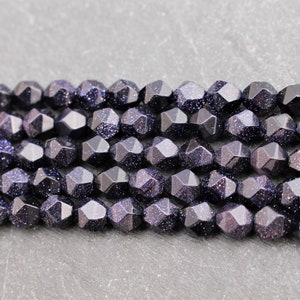 Pode incluir: Close-up de contas de arenito azul escuro facetadas com inclus&otilde;es brilhantes. As contas s&atilde;o enfiadas, perfeitas para criar joias como colares e pulseiras.