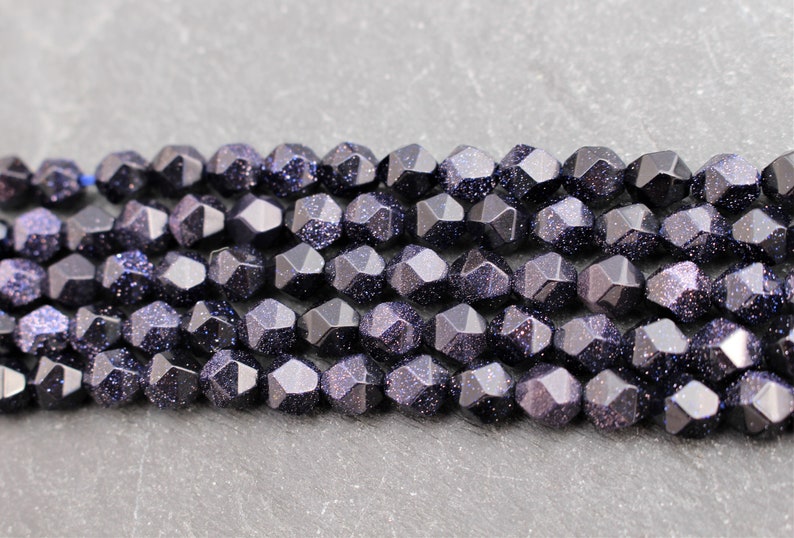 Pode incluir: Close-up de contas de arenito azul escuro facetadas com inclus&otilde;es brilhantes. As contas s&atilde;o enfiadas, perfeitas para criar joias como colares e pulseiras.