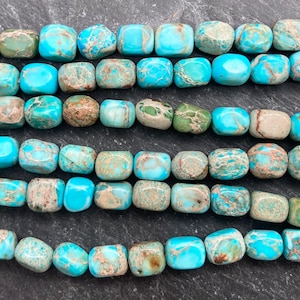 May include: Close-up of turquoise, green, and brown square beads. The beads are strung together, possibly for jewellery making. The beads have a slightly irregular shape and a matte finish. The colours vary across the beads.