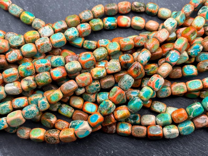 Pu&ograve; includere: Fili di perline quadrate nei toni del turchese, arancione, marrone e giallo. Le perline hanno un aspetto maculato di pietra naturale. Le perline sono infilate insieme, creando un'esposizione strutturata e colorata. Ideale per la creazione di gioielli.