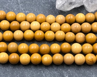 Può includere: Primo piano di fili di perline rotonde e lucide in varie tonalità di giallo e beige. Le perline sono uniformi per dimensioni e forma, con una finitura liscia e lucida. Le perline vengono probabilmente utilizzate per la creazione di gioielli.