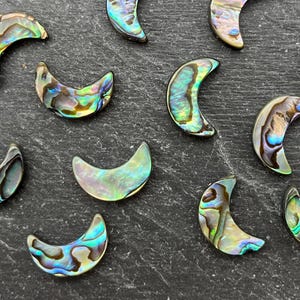 May include: A collection of iridescent abalone shell crescent moon shapes. The shells display a range of colors, including blues, greens, and golds, with a shimmering, pearlescent effect. These decorative pieces are ideal for jewelry making or craft projects.