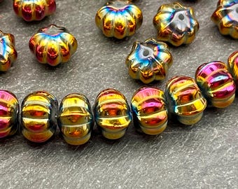 Può includere: Una collezione di piccole perline a forma di zucca con una vibrante finitura arcobaleno iridescente. Ogni perlina mostra una lucentezza metallica con tonalità cangianti di oro, magenta e blu, e include un foro centrale per l'infilatura.