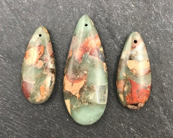 Pode incluir: Três pingentes em forma de gota com um furo na parte superior. Os pingentes apresentam um padrão manchado de verde, vermelho e bege. Os pingentes são de tamanhos diferentes, o maior tem cerca de 7,6 cm de comprimento.