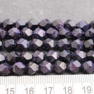 Pode incluir: Close-up de um fio de contas facetadas azul escuro com inclus&otilde;es brilhantes. As contas est&atilde;o dispostas em fileiras ordenadas, e uma r&eacute;gua &eacute; vis&iacute;vel na parte inferior, indicando o seu tamanho. Estas contas s&atilde;o adequadas para fazer joias.