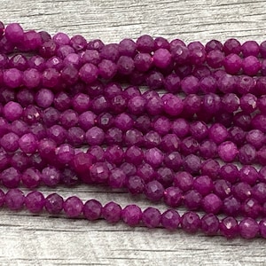 May include: Strands of faceted, deep magenta gemstone beads. The beads have a multi-faceted surface, catching the light and creating a sparkling effect. These beads are strung together, ready for jewelry making or other craft projects.