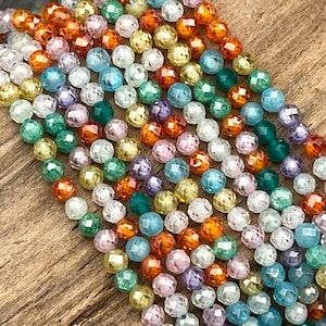 May include: A collection of small, round, faceted beads arranged in multiple parallel strands. The beads feature a translucent finish and a vibrant spectrum of colors, including shades of orange, yellow, green, blue, purple, and clear white.