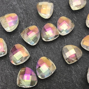 May include: Close-up of several iridescent, triangular-shaped beads. The beads have a faceted surface that reflects a spectrum of colors, including pink, yellow, and green. They are scattered on a dark, textured surface.