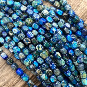 May include: Close-up of a collection of blue and green gemstone beads. The beads have a mix of colors and patterns, with shades of blue, teal, and green. The beads are strung together, creating a textured and colorful display. Ideal for jewelry making.