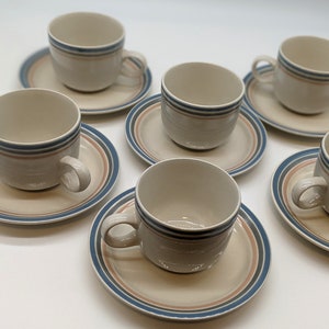May include: Six white ceramic teacups with blue and pink stripes, each on a matching saucer with blue and pink stripes.