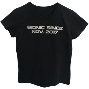 May include: Black t-shirt with silver lettering that reads "Bionic Since Nov. 2017".