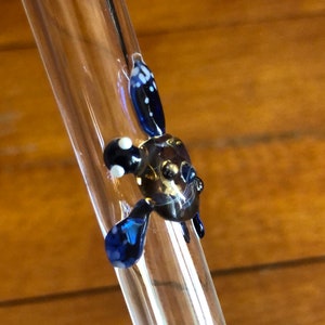 May include: A glass drinking straw with a blue and white glass turtle design at the top.