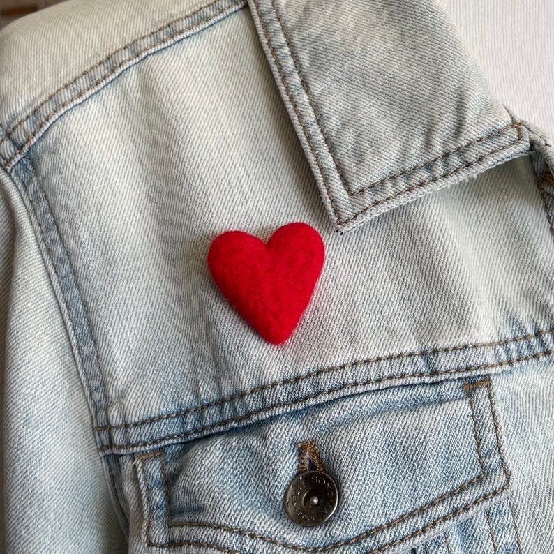 May include: A red felt heart pinned to a denim jacket.
