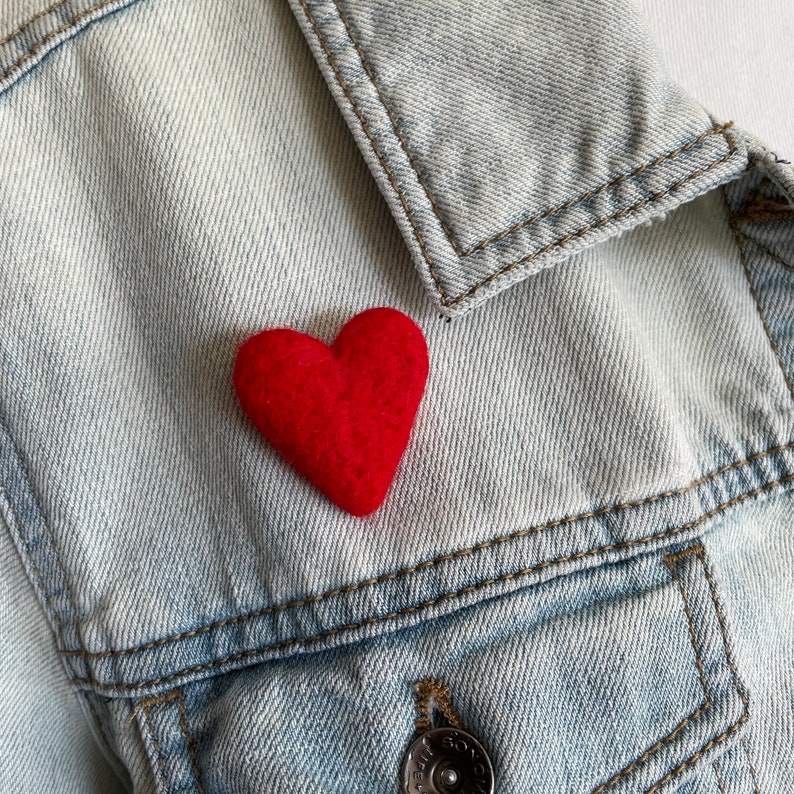 May include: A red felt heart pinned to a light blue denim jacket.