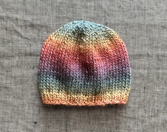 May include: A hand-knitted beanie hat in a rainbow of colors, including yellow, orange, pink, purple, blue, and green. The hat is made of soft yarn and has a ribbed brim. The hat is a cozy accessory for cold weather.