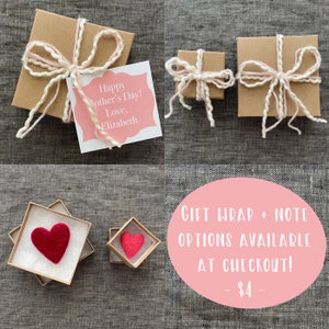 May include: Two small gift boxes wrapped in brown paper with pink and white twine bows. A card with the text "Happy Mother's Day! Love, Elizabeth" is in the background. The text "GIFT WRAP + NOTE OPTIONS AVAILABLE AT CHECKOUT! - $4 -" is in a pink circle.