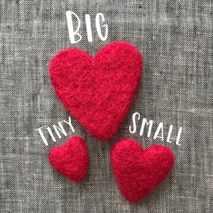 May include: Three red felt hearts of different sizes on a gray fabric background. The largest heart is labeled "BIG", the middle heart is labeled "TINY", and the smallest heart is labeled "SMALL".