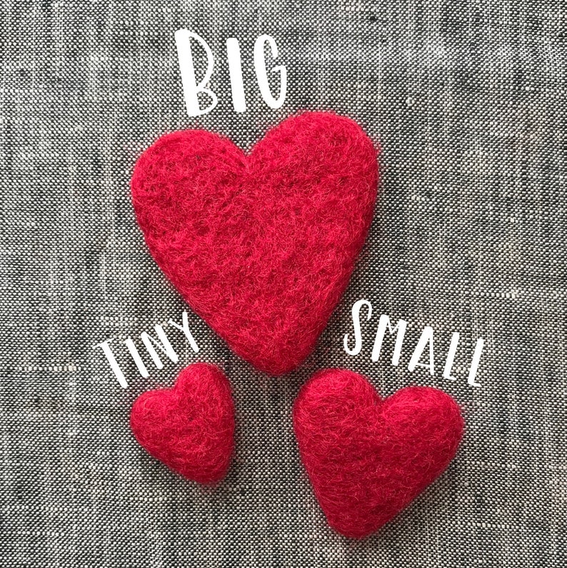 May include: Three red felt hearts of different sizes on a gray fabric background. The largest heart is labeled "BIG", the middle heart is labeled "TINY", and the smallest heart is labeled "SMALL".