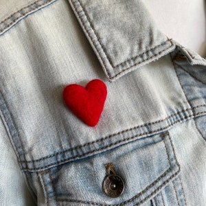 May include: A red felt heart pinned to a light blue denim jacket.