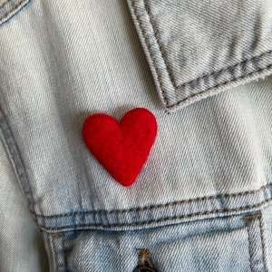 May include: A red felt heart pinned to a light blue denim jacket.
