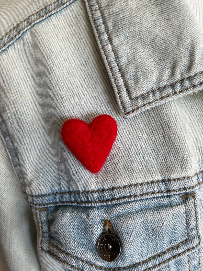 May include: A red felt heart pinned to a light blue denim jacket.
