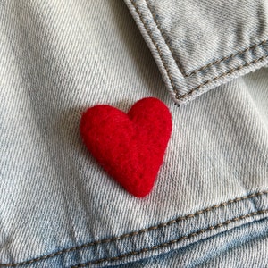 May include: A red felt heart pinned to a light blue denim jacket.