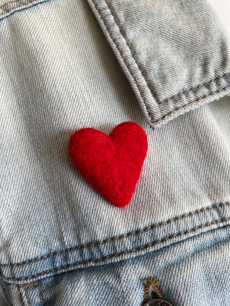 May include: A red felt heart pinned to a light blue denim jacket.