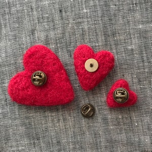 May include: Three red felt heart-shaped pins with gold metal pin backs. The hearts are different sizes.
