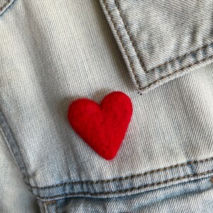 May include: A red felt heart pinned to a light blue denim jacket.
