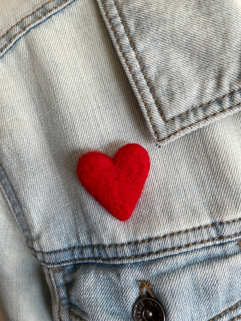 May include: A red felt heart pinned to a light blue denim jacket.