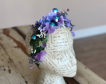 May include: Purple and white flower crown with turquoise mushroom accents. The crown is on a white mannequin head.