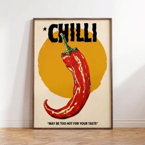 Puede incluir: Un póster enmarcado con un pimiento rojo vibrante sobre un fondo amarillo en forma de sol. El texto negro en negrita en la parte superior dice "CHILLI", con la frase "MAY BE TOO HOT FOR YOUR TASTE" en la parte inferior. El póster tiene un estilo vintage.