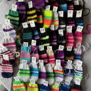 May include: A collection of 46 colorful crocheted pouches with striped patterns. Each pouch has a number tag attached to it.
