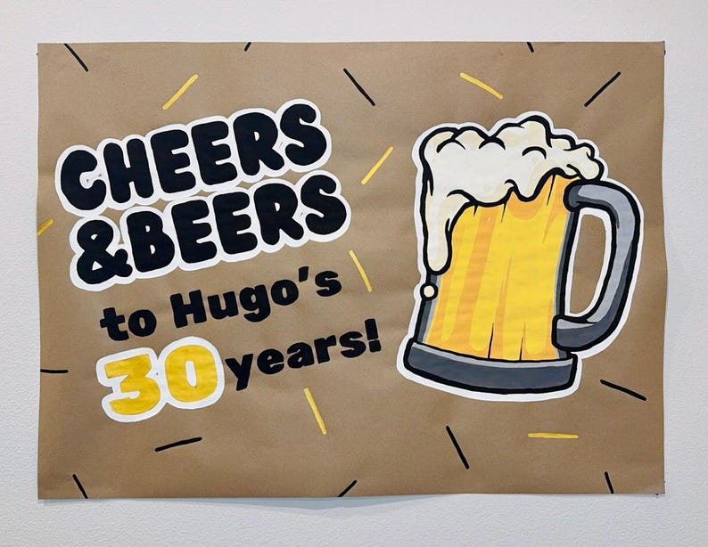 Puede incluir: Un letrero de papel marr&oacute;n con las palabras "CHEERS & BEERS" en negrita, en negro, y "to Hugo's 30 years!" en una fuente m&aacute;s peque&ntilde;a. Una jarra de cerveza de dibujos animados con espuma est&aacute; a la derecha, con detalles en amarillo y negro.