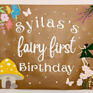 Puede incluir: Un letrero marr&oacute;n con el texto "Sylia's fairy first Birthday" en escritura blanca. El letrero est&aacute; decorado con flores coloridas, mariposas, una casa de champi&ntilde;ones amarilla y una ilustraci&oacute;n de hadas.