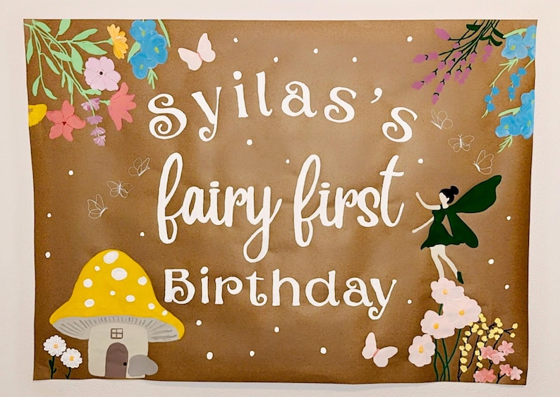 Puede incluir: Un letrero marr&oacute;n con el texto "Sylia's fairy first Birthday" en escritura blanca. El letrero est&aacute; decorado con flores coloridas, mariposas, una casa de champi&ntilde;ones amarilla y una ilustraci&oacute;n de hadas.