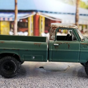 May include: A green vintage pickup truck with black wheels and a weathered, rusty roof. The truck has a detailed design, including a Ford emblem on the front. The truck is a miniature model, likely a collectible item.